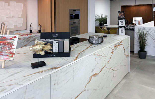 Foto aus der Ausstellung des Küchenstudios auf Mallorca: Weiße Kochinsel vor einer Küchenzeile mit Hochschränken aus Holz.