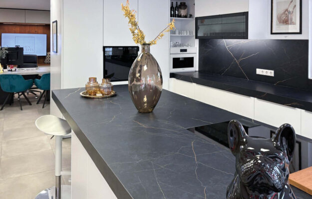 Foto der Ausstellung des Küchenstudios: Weiße L-Küche mit Kochinsel und schwarzer Steinarbeitsplatte.